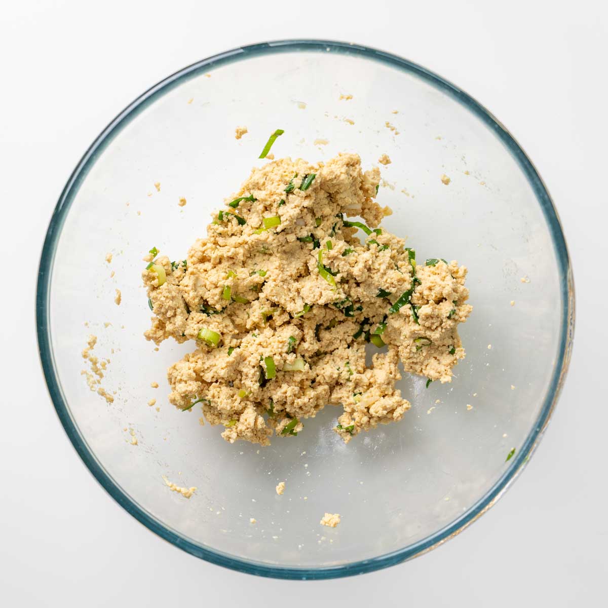 Crumbled tofu filling mixed with chopped scallions, ginger, tamari, and maple syrup in a glass bowl