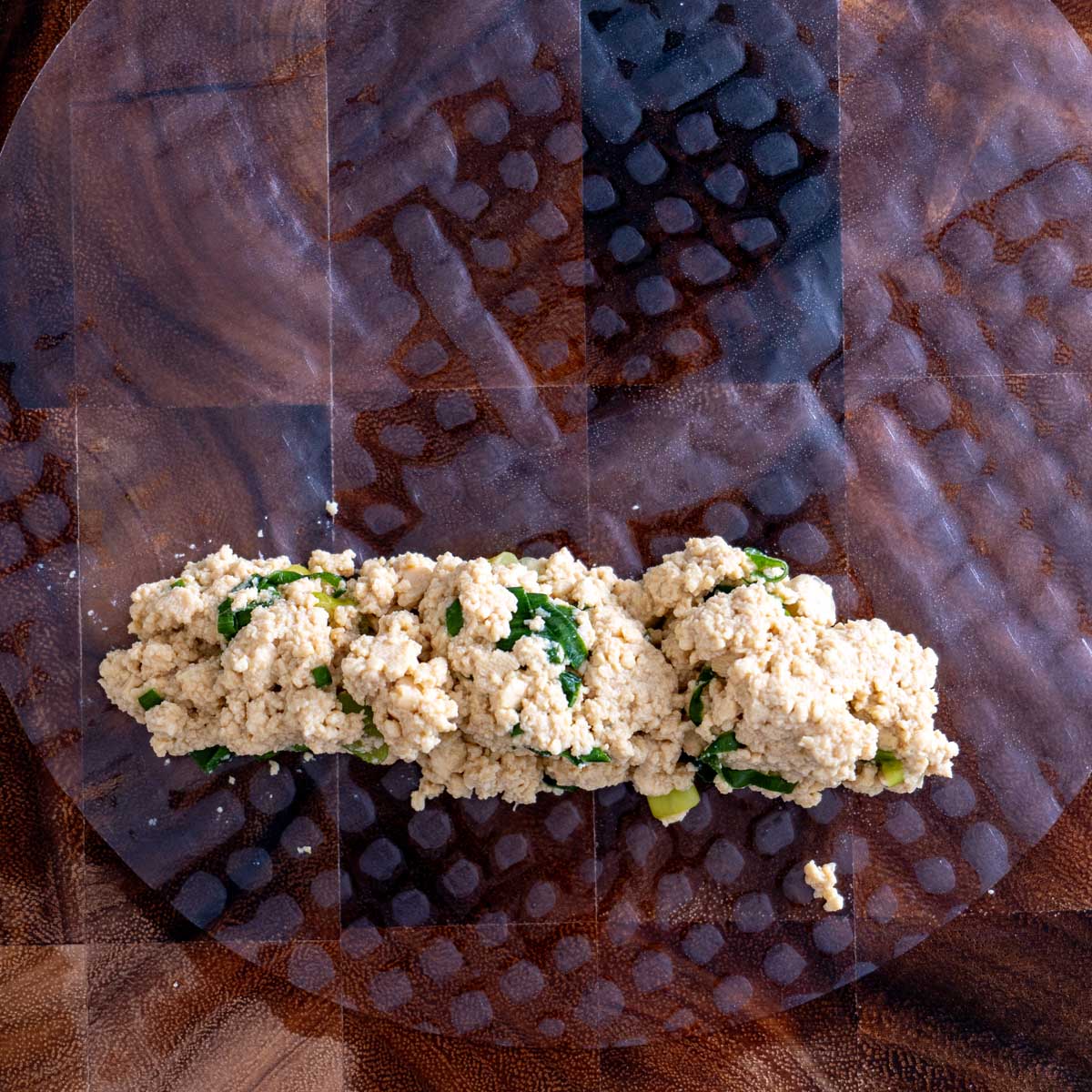 Seasoned tofu filling shaped into a long sausage across the lower third of a softened rice paper sheet on a wet wooden board