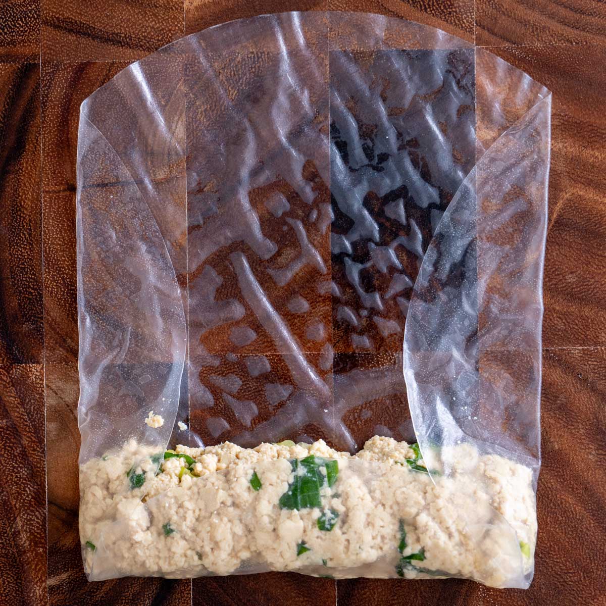 Rice paper wrapped tightly around the tofu filling on a wet wooden board, sealed and ready to cut into nuggets