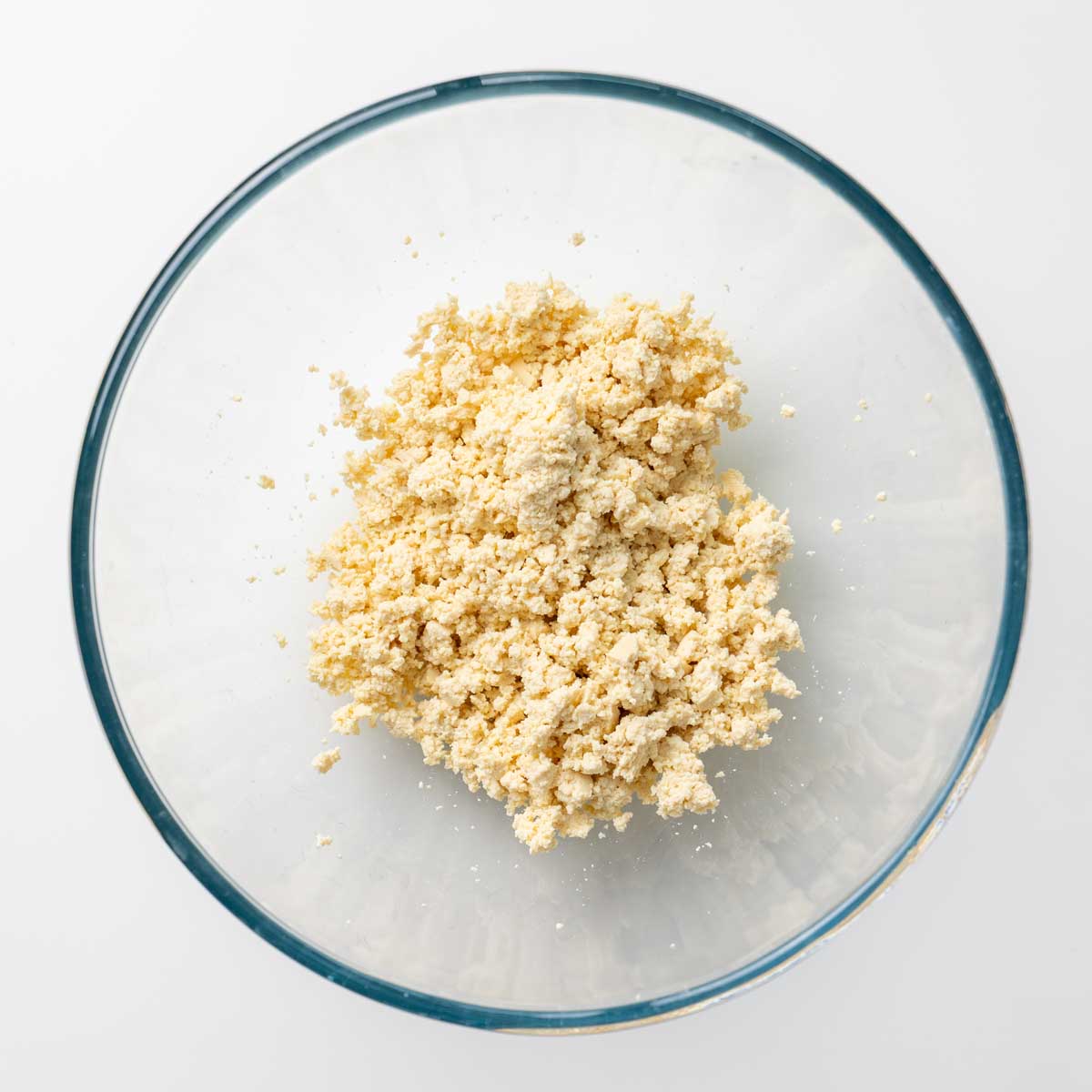 Extra-firm tofu crumbled finely into a glass mixing bowl, ready to be seasoned for the rice paper nugget filling