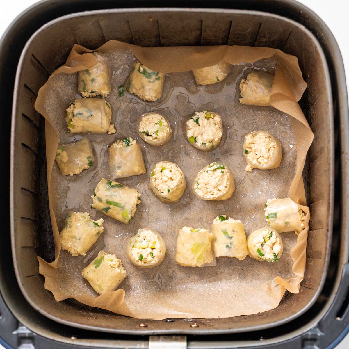 Bite-sized rice paper nuggets spaced out on baking paper in an air fryer basket before cooking