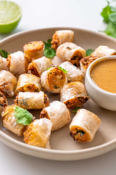 Viral crispy rice paper nuggets on a cream plate with a small bowl of spicy peanut dipping sauce, topped with fresh cilantro and a lime half alongside