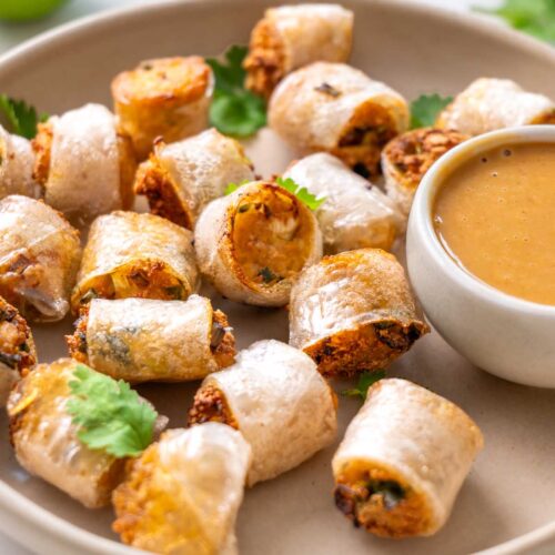 Viral crispy rice paper nuggets on a cream plate with a small bowl of spicy peanut dipping sauce, topped with fresh cilantro and a lime half alongside