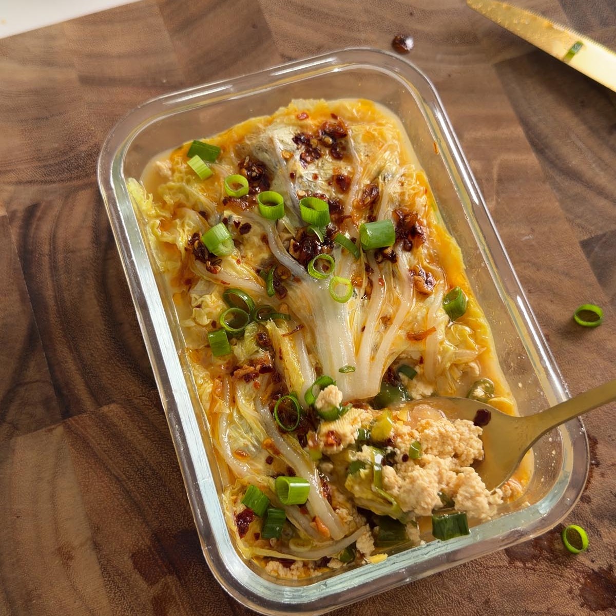 cabbage soup dumpling lasagna in a glass dish with a spoonful taken out, topped with crispy chili oil and scallions.