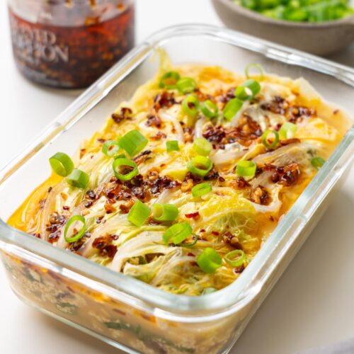 cabbage soup dumpling lasagna in a glass dish on a white surface, topped with crispy chili oil and scallions.