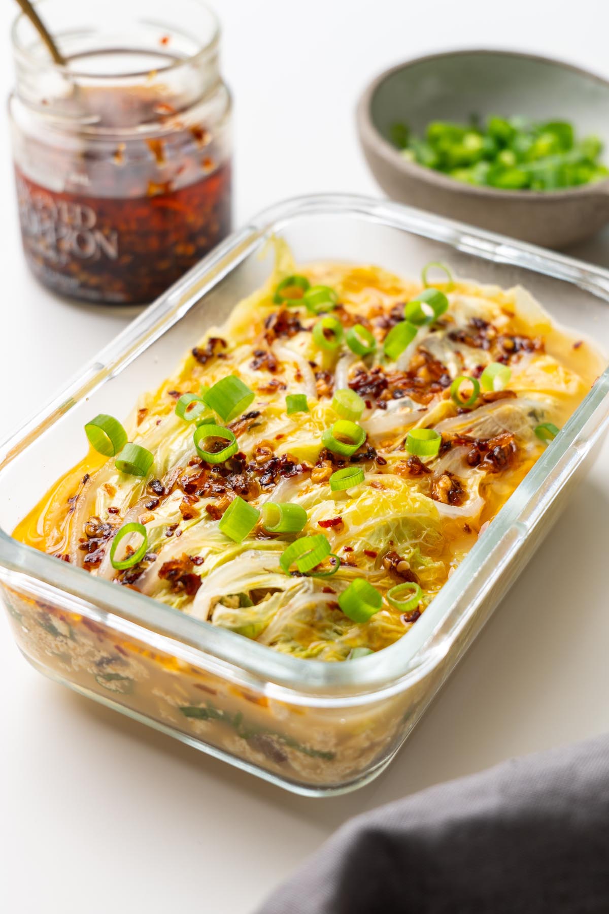 cabbage soup dumpling lasagna in a glass dish on a white surface, topped with crispy chili oil and scallions.