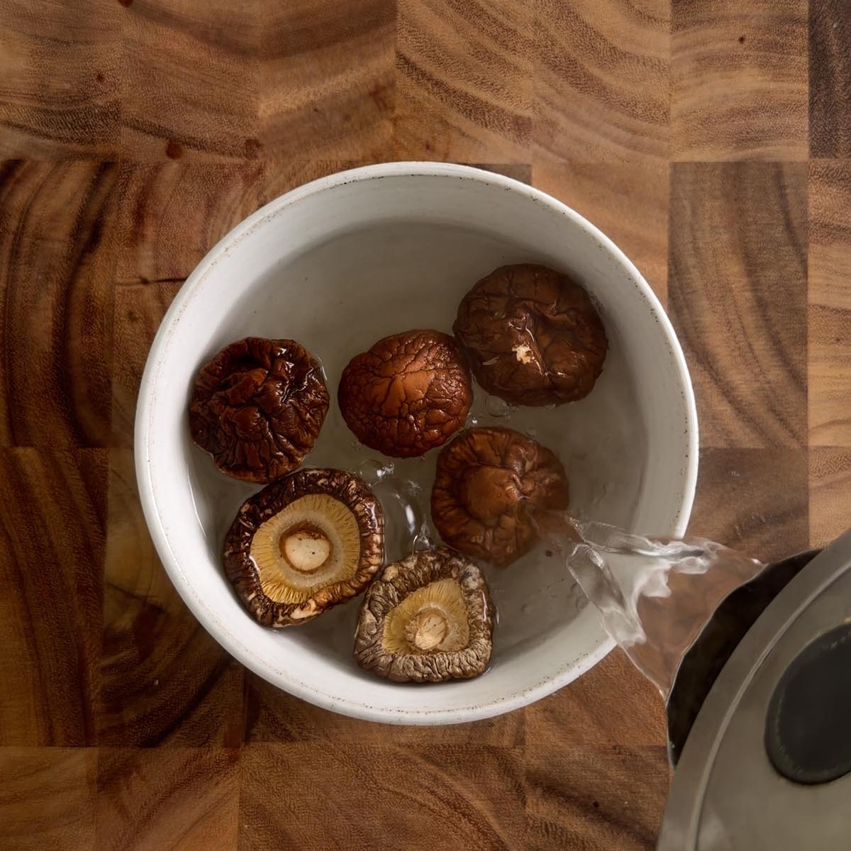 dried shiitake mushrooms in a bowl with boiling water being poured over them.
