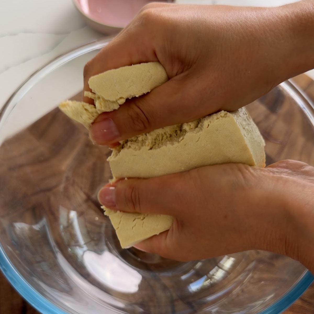 Sarah Cobacho crumbling extra-firm tofu into a glass mixing bowl.