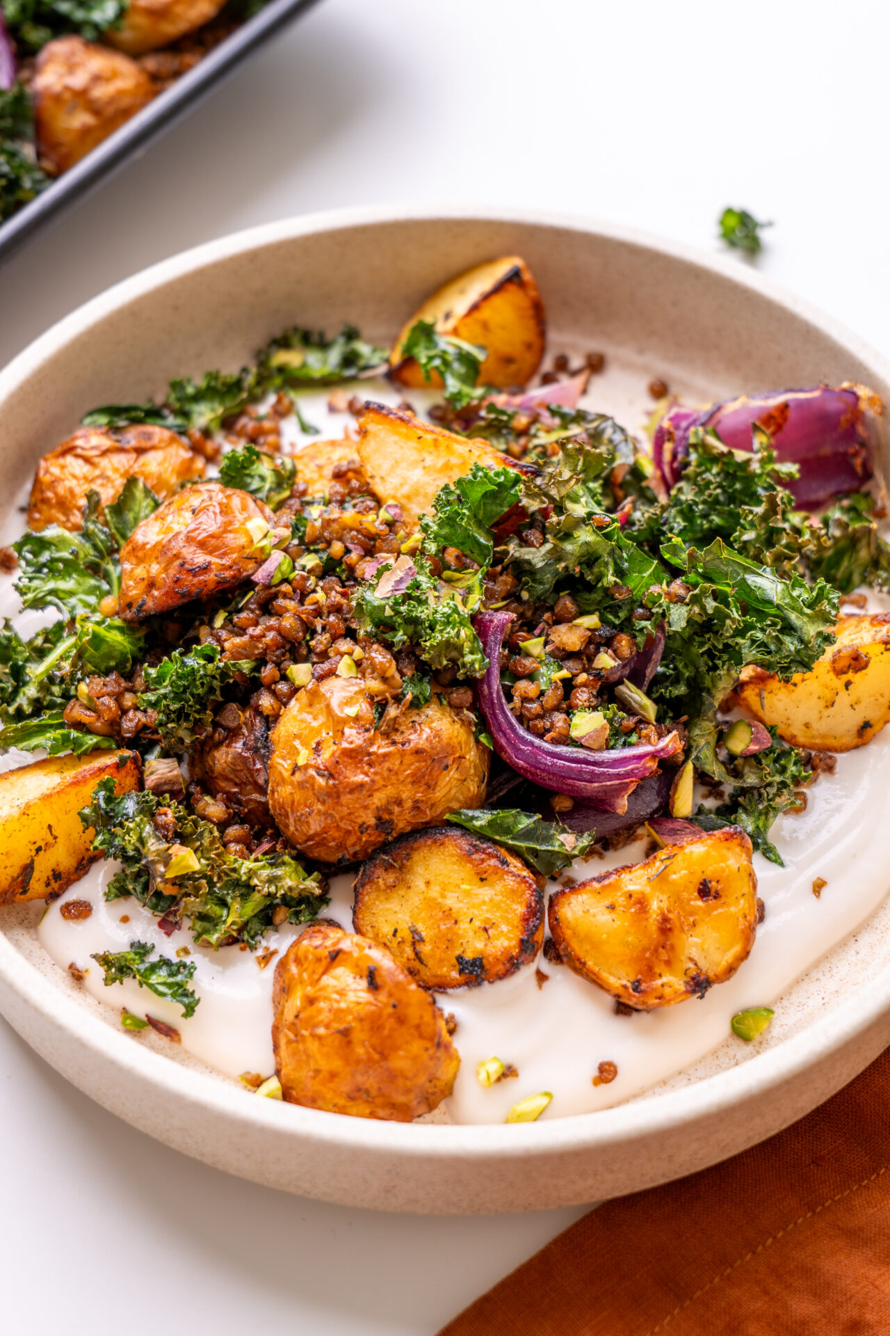Sheet Pan Potato and Crispy Kale Bowl plated with tahini yogurt sauce and pistachios.