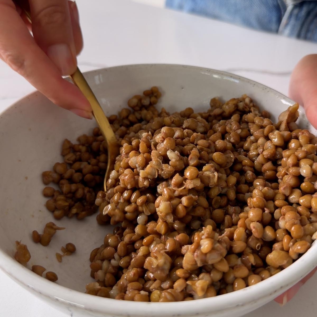 mixing olive oil into cooked brown lentils in a bowl.