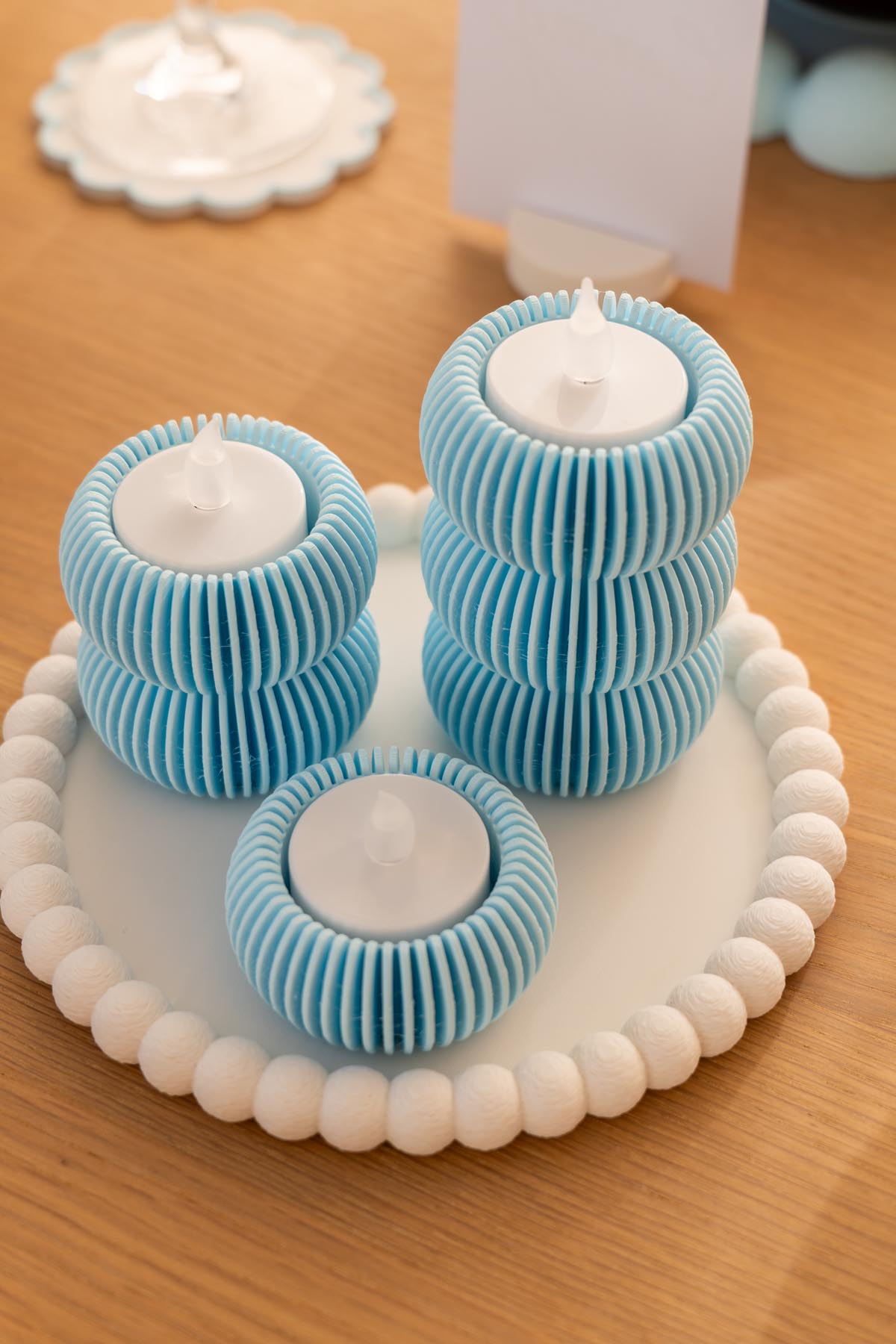 Three 3D printed baby blue fluted tea light holders at different heights on a white beaded dish