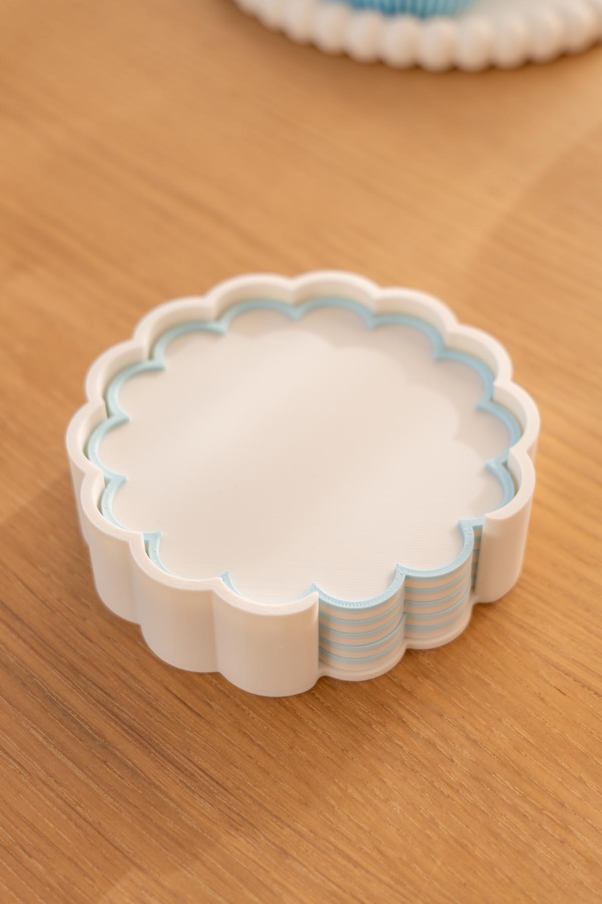 A stack of 3D printed white scalloped coasters with blue edges sitting inside a matching scalloped holder