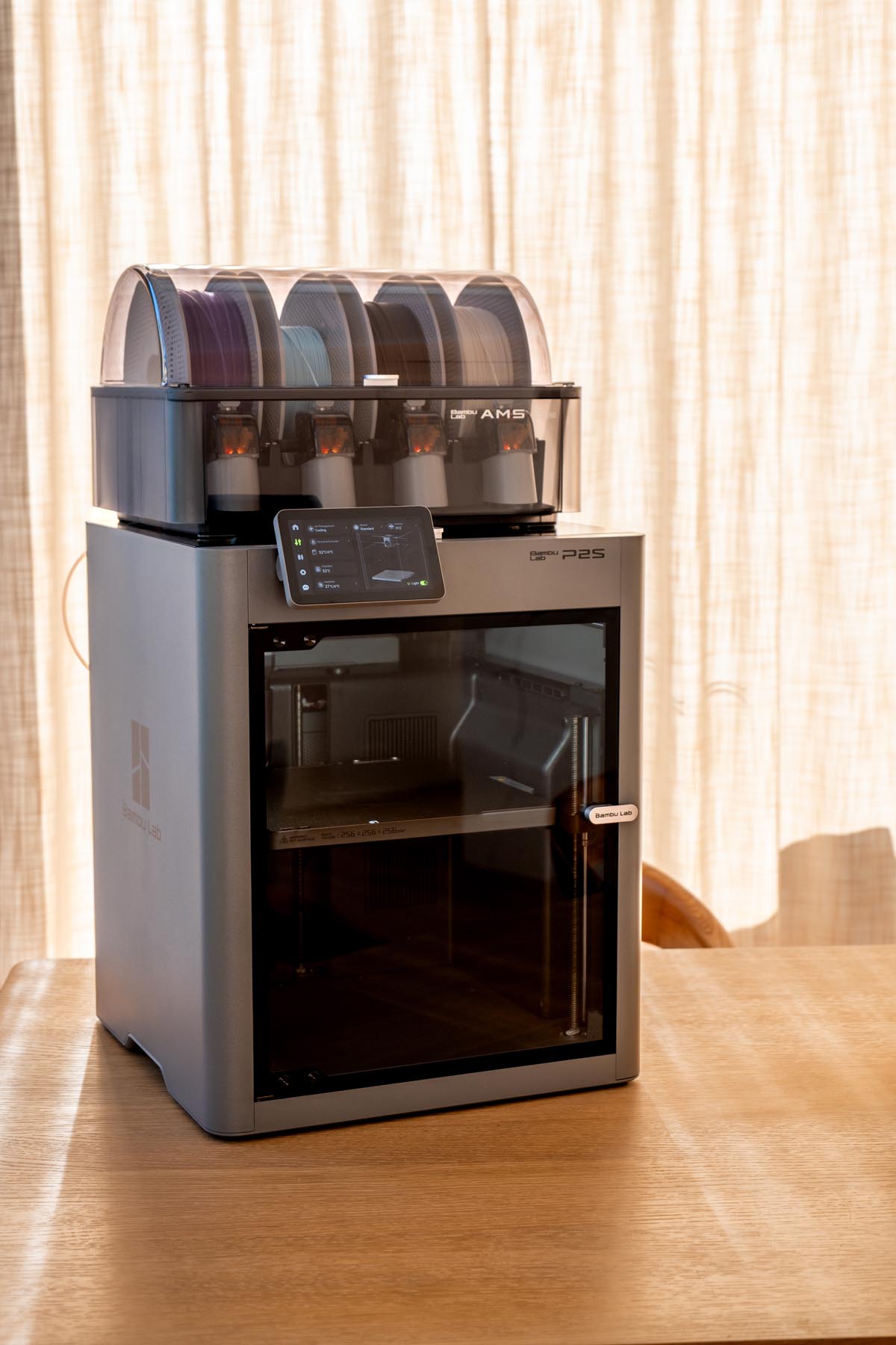 A Bambu Lab P2S 3D printer with the AMS multi-color unit on top, loaded with four spools of filament