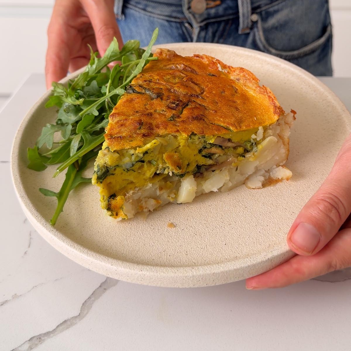 Sarah Cobacho holding a plate of vegan potato crust quiche with a side of arugula.