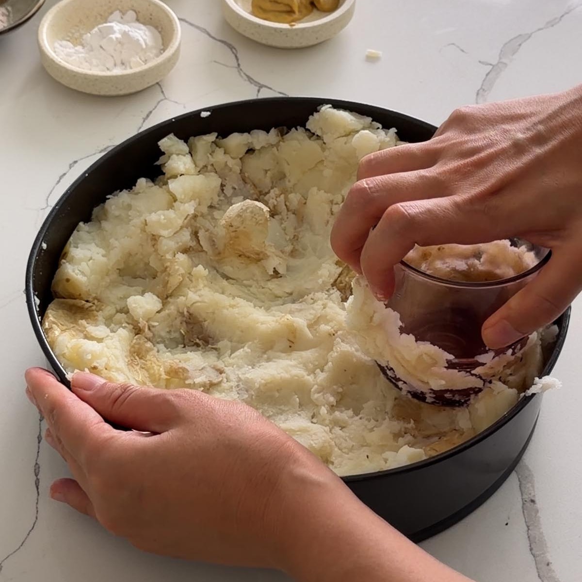 Sarah Cobacho pressing boiled potatoes into a springform pan with the bottom of a glass.
