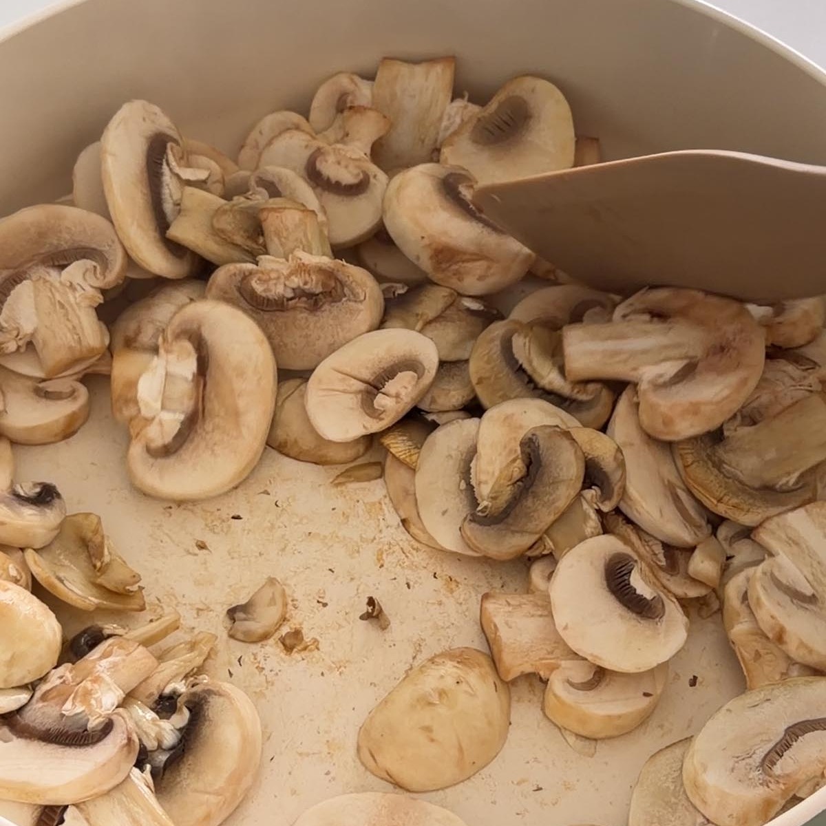 sliced button mushrooms cooking in a dry pan over medium heat.